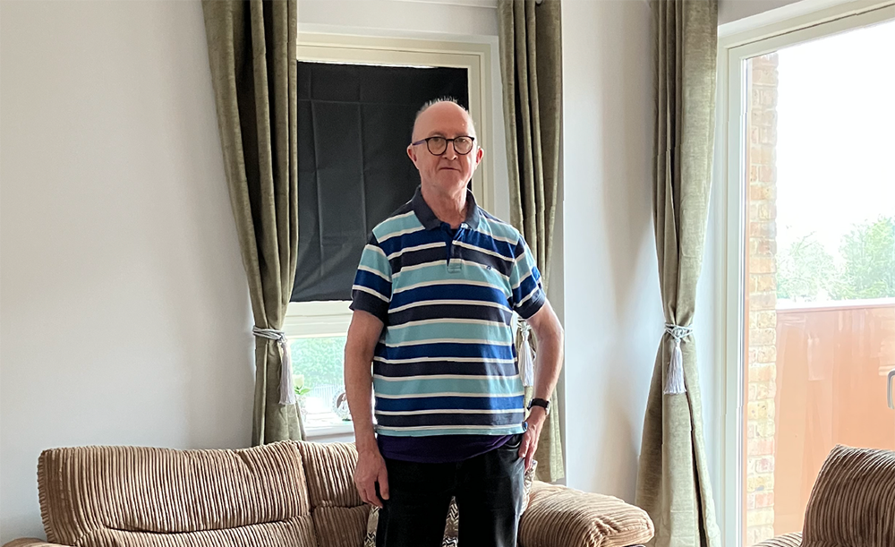 Eric standing in a living room, wearing a polo shirt and glasses.