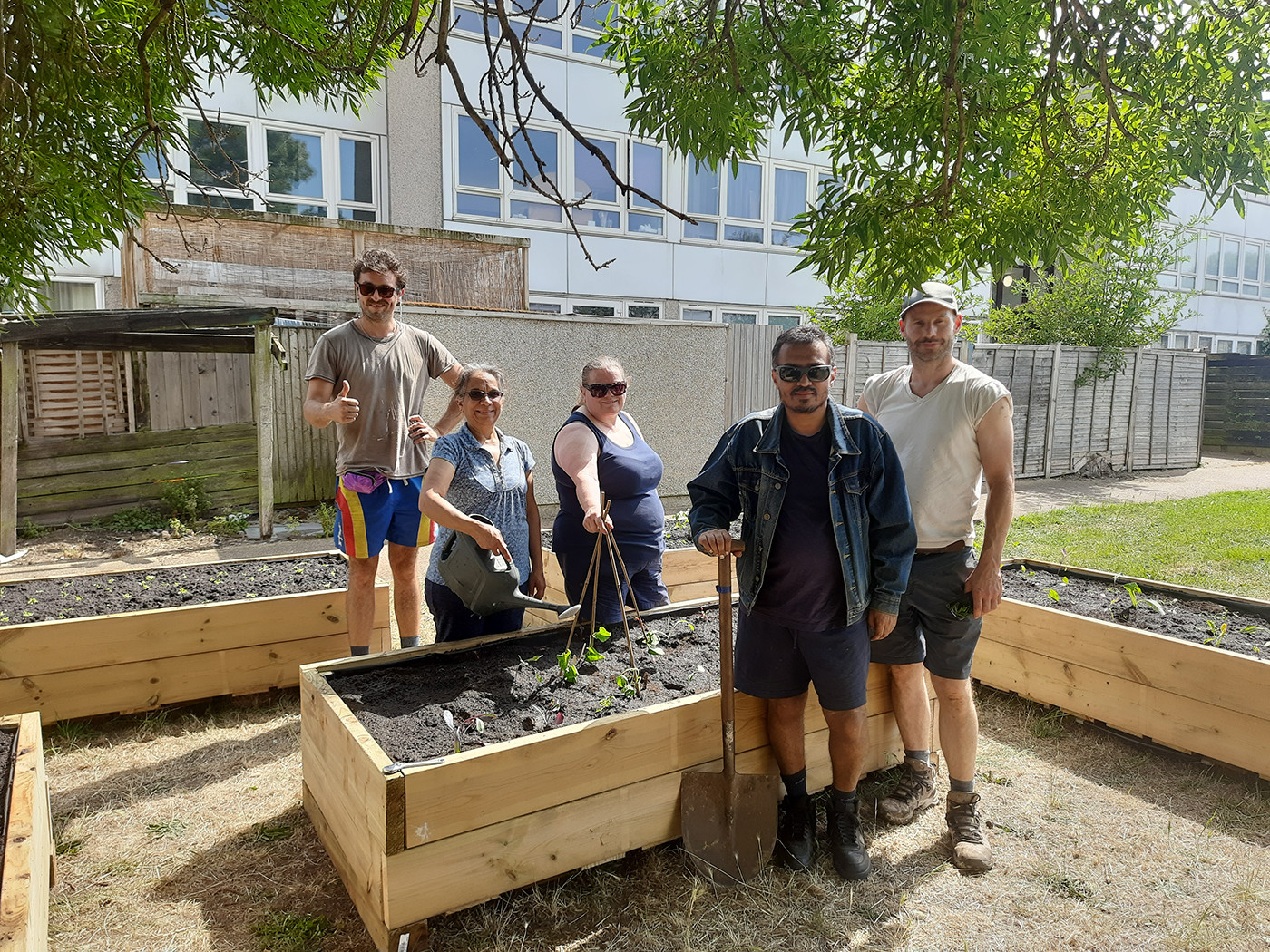 5 people stand in front of some newly built raised planters, holding spades. The Eastfields estate is in the background.